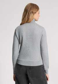 Felpa grigia a maniche lunghe con colletto alto, bordo a coste e polsini, realizzata in un morbido tessuto testurizzato e con una silhouette aderente.