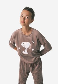 Brun fleece loungewear sæt med et Snoopy grafik på toppen. Bukserne har et gentagende Snoopy ansigt mønster, komplet med en elastisk talje.