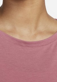 Nahaufnahme des Nackens und oberen Brustbereichs einer Person, die ein pinkes Rundhals-Shirt trägt, vor einem weißen Hintergrund.