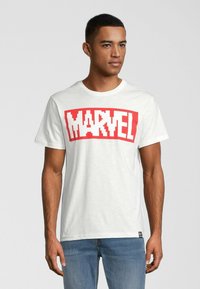 Hvid bomulds t-shirt med et fedt rødt "MARVEL" logo i pixeliseret skrifttype. Har rund hals og korte ærmer. Bæres med blå jeans.