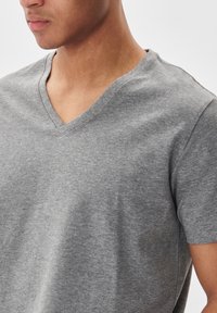 T-shirt grigio a V in un tessuto morbido e elasticizzato. Presenta maniche corte e una vestibilità morbida, con una texture liscia e uniforme.