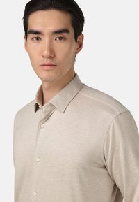 Beżowa koszulka polo z kołnierzykiem, o gładkiej fakturze i czterema guzikami z przodu. Krótkie rękawy o luźnym kroju.