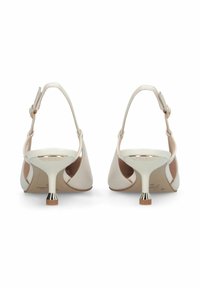 Paire d'escarpins beige à talons kitten avec brides arrière et petites touches métalliques sur les bouts des talons, présentés de dos sur un fond blanc.