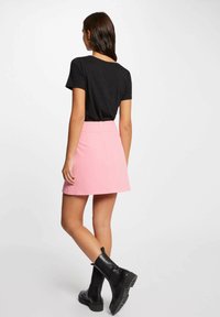 T-shirt nero a maniche corte abbinato a una mini gonna rosa, con zip sul retro. Indossato con stivaletti neri alla caviglia e suola texturizzata.