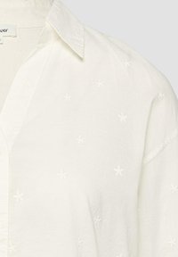 Chemise blanche à col avec de subtils petits motifs floraux brodés répartis uniformément sur le tissu.