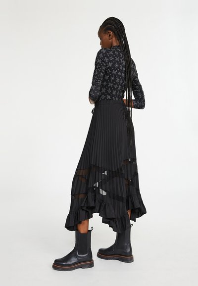 Zwarte geplooide rok met een gerimpelde rand en doorschijnende panelen, gecombineerd met een aansluitende zwart long-sleeve top met een patroon en enkellaarsjes.
