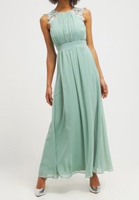 Mint vihreä maksimekko, jossa on pleatattu rintakappale, kukkakuvioista pitsiä hartioilla ja laskeutuva hame. Yhdistetty hopeisiin metallisiin kenkiin.