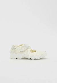 White athletic shoe with mesh upper, cushioned midsole, and velcro strap. Features rounded toe and rubber outsole for grip.