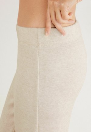 Leggings beiges avec un tissu texturé, taille haute, et sans coutures visibles, avec un gros plan de la taille et une main ajustant l'ajustement.
