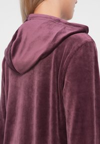 Paarse plush hoodie met een zachte textuur en een gladde afwerking, voorzien van een strakke capuchon en nette stiksels.