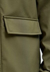 Veste vert olive dotée d'une poche à rabat horizontale, réalisée en tissu lisse et ornée de bords cousus.