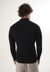 Maglione nero a trecce con collo alto, polsini e orlo a costine. Presenta un motivo testurizzato e una silhouette aderente sul retro.