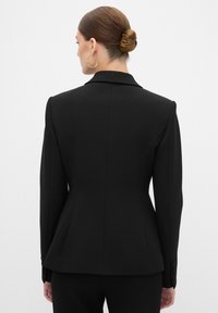 Svart skräddarsydd blazer med en figursydd design, strukturerade axlar, lätt utsvängd fåll och knäppta ärmar. Slät tygkvalitet.