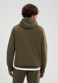 Oliwkowy hoodie z dużym, podwójnym kapturem, prążkowanymi mankietami i luźnym krojem, wykonany z miękkiej, teksturowanej mieszanki bawełny.