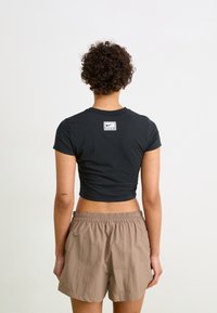 Črna skrajšana majica iz mehke tkanine, ki ima na zgornjem delu hrbta majhno belo oznako Nike; kombinirana z bež hlačami z elastičnim pasom.