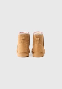 Bottines en daim beige avec un bout arrondi, un intérieur doux et une couture contrastante rose et blanche le long du bord.