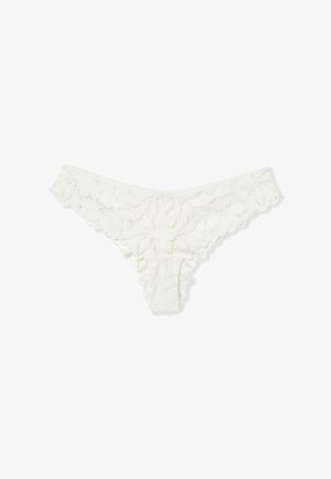 Tanga de encaje blanco con patrones florales, bordes con bordado en forma de concha y una cinturilla de tiro bajo sobre un fondo blanco liso.