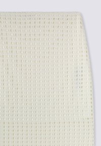 Tessuto bianco texturizzato con un motivo a griglia e punti in rilievo, creando una superficie tattile. Il materiale sembra morbido e traspirante.