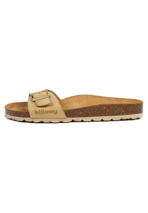 Sandale beige à enfiler avec un pied en relief, une semelle en liège et une sangle réglable avec une boucle. La marque est embossée sur la sangle.