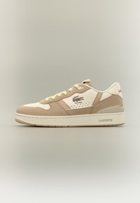 Pantofii sport Lacoste prezintă un amestec de piele crem și bej, cu o textură netedă, vârf rotund, șireturi galbene deschise și branding pe laterale și în partea din spate.
