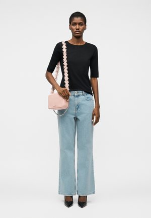 Γυναίκα που στέκεται φορώντας μαύρο τοπ με μανίκια μέχρι τον αγκώνα, ανοιχτό μπλε τζιν με φαρδιά πόδια, μαύρα μυτερά τακούνια και κρατώντας μια ανοιχτό ροζ τσάντα με λουλουδάτο λουράκι.