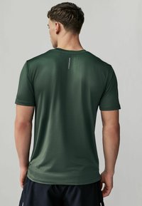 Grøn kortærmet atletisk T-shirt med et struktureret mønster, rund hals og reflekterende detaljer på ryggen. Letvægts, tætsiddende design.
