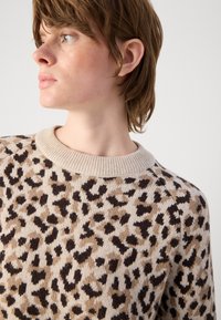 Beige Strickpullover mit einem Leopardenmuster in Braun und Schwarz. Verfügt über einen gerippten Rundhalsausschnitt und eine lockere Passform. Weiche Textur.
