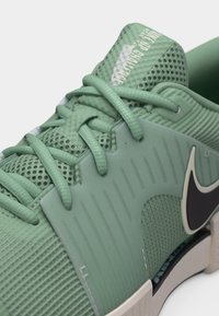 Κοντινή λήψη πράσινου αθλητικού παπουτσιού με πλέξη στο άνω μέρος, υφασμένα κορδόνια, επενδεδυμένη γλώσσα με την ετικέτα "NIKE GP CHALLENGE" και εμφανές μαύρο λογότυπο Nike.