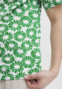 Kortermet skjorte med et grønt blomstermønster på hvit bakgrunn. Materialet er lett og har en myk tekstur.