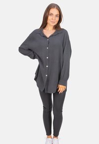 Dark gray, oversized button-up shirt in textured fabric with a collar and long sleeves, paired with black leggings and white sneakers.