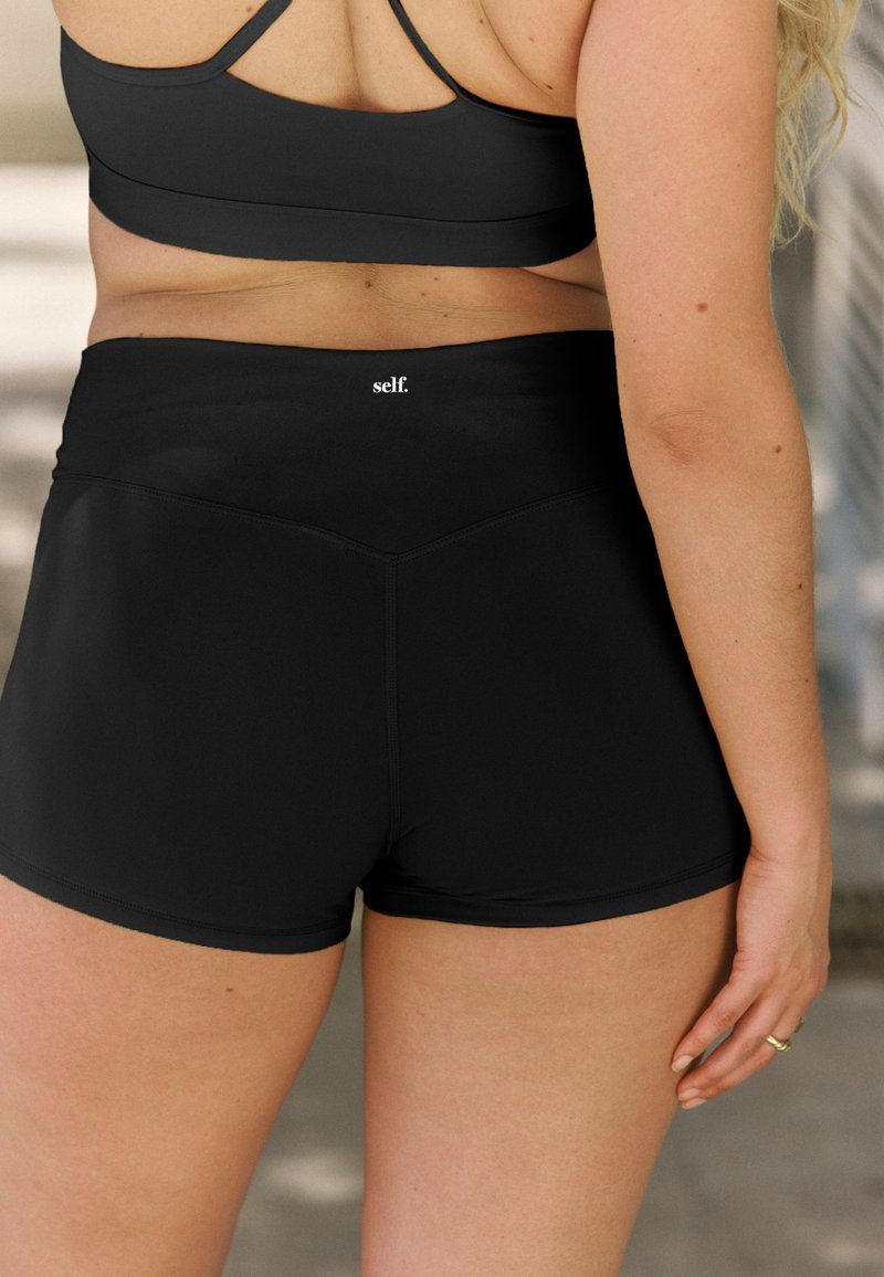 Pantaloncini sportivi neri con vita alta, realizzati in tessuto liscio ed elastico. Presentano un logo sottile sul retro e un design aderente.