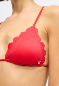 Κόκ�κινο τοπ μπικίνι με φιλντισένιες άκρες, λεπτούς ρυθμιζόμενους ιμάντες και συγκεντρωμένα cups. Το υλικό φαίνεται λείο και ελαστικό με ελάχιστη σήμανση.