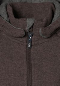 Brun zip-up jacka med hög krage, mjukt grått innerfoder och en dekorativ dragkedja med unika mönsteraccenter.