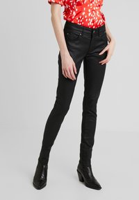 Jeans negros ajustados con una textura suave y diseño de cinco bolsillos, complementados con una blusa entallada blanca con lunares rojos y botas negras de tacón.