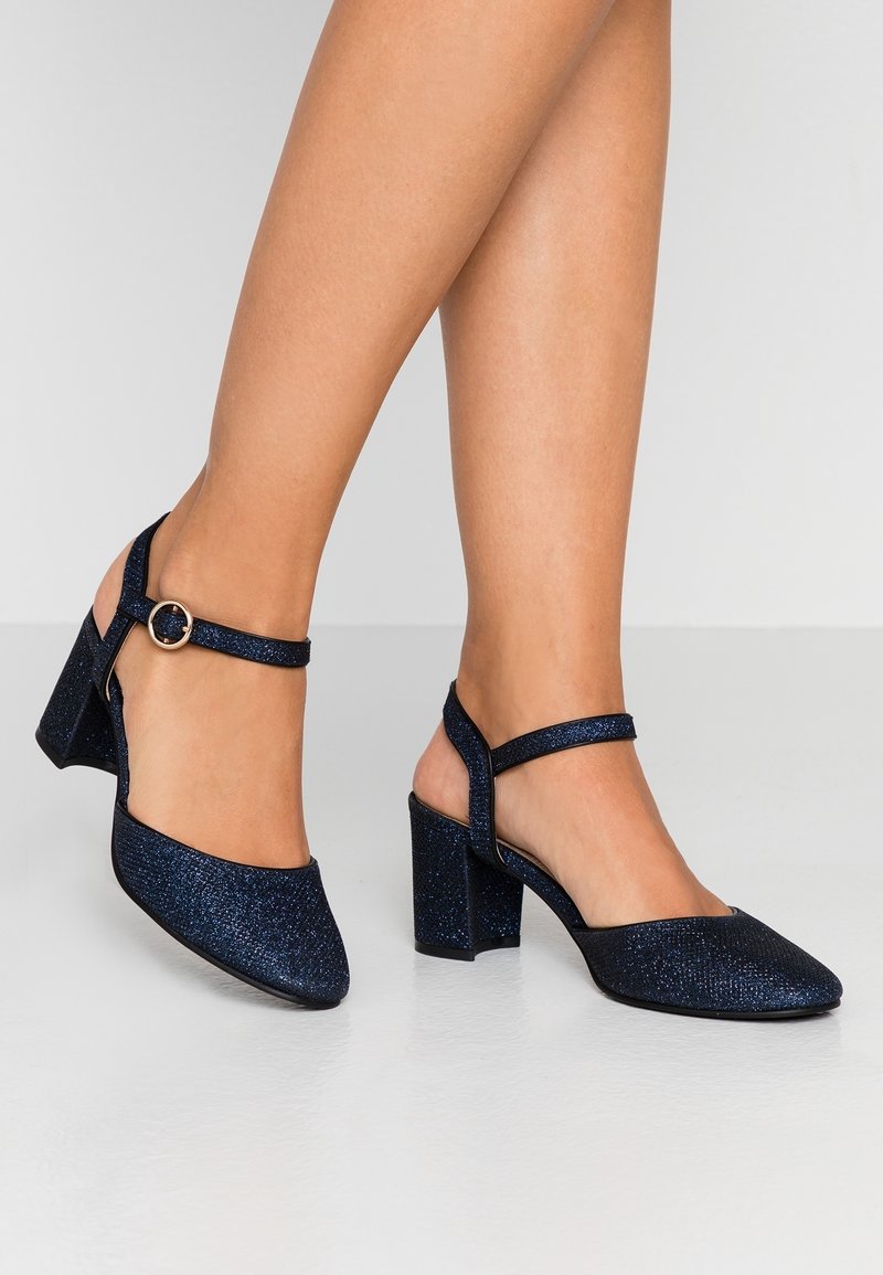 Mörkblå, glittriga slingback-hälar med rund tå, blockklack och ett smalt ankelsnöre med en cirkulär metallspänne.