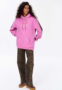 Přessize růžová mikina s klokaní kapsou a šňůrkami, kombinovaná s hnědými a černými kalhotami s leopardím potiskem a rozšířenými nohavicemi. Hnědé akcenty na rukávech.