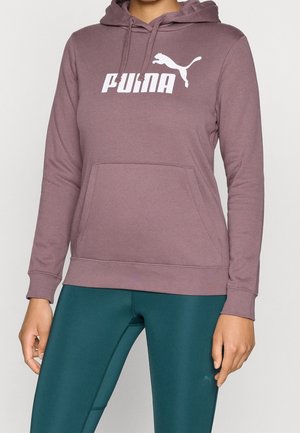 Personne portant un sweat à capuche mauve Puma avec poche avant et des leggings bleu canard foncé.