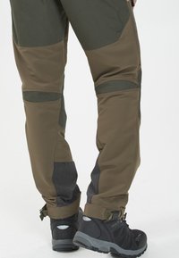 Vaellushousut oliivinvihreinä ja ruskeina, joissa on päällystetty suunnittelu, hengittävät verkko-ominaisuudet ja säädettävät lahkeet. Yhdistetty mustiin vaelluskengiin.