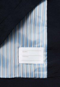 Tejido de un azul marino oscuro con un forro a rayas en azul claro y blanco. Se puede ver una etiqueta en blanco con campos para "NOMBRE" y "TELÉFONO."