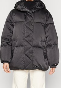 Svart pufferjacka med huva, med diagonala sömmar, elastiska ärmslut och dragkedjestängning. Tillverkad av ett glatt, glansigt material.