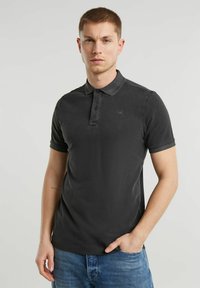 Polo shirt grigio scuro in cotone, con placca di bottoni, maniche corte e un logo discreto sul petto. Indossato con jeans blu.