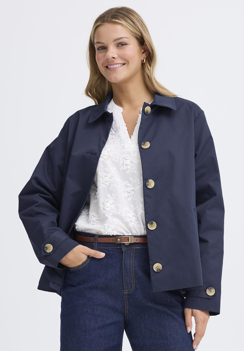 Tamsiai mėlyna, lengvo audinio užsegama striukė su aukso spalvos sagomis, apykakle ir laisvo kirpimo. Dėvima ant baltos palaidinės.