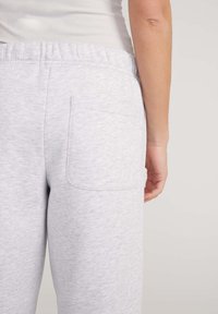 Pantaloni della tuta grigi chiari realizzati in tessuto morbido, con un elastico in vita e una sola tasca posteriore, dotati di una texture liscia e di una vestibilità comoda.