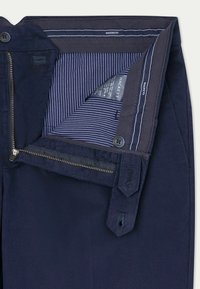 Pantalon bleu marine avec une fermeture éclair, doublure intérieure rayée, fermeture à bouton, et coutures détaillées le long de la ceinture et des poches.