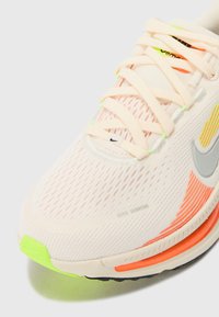 Light pink running shoe with mesh upper, reflective accents, and neon yellow, orange, and green details. Features white laces and a rubber sole.