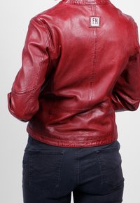 Chaqueta de cuero roja con una textura suave, costuras en los hombros y un parche con logo. Combinada con jeans oscuros de color navy que cuentan con bolsillos traseros.