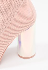Botín de punto rosa hasta el tobillo con un tacón de bloque holográfico, que presenta una superficie texturizada y acentos lisos en la base para añadir un detalle extra.