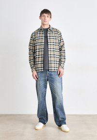 Checkered shirt in beige and navy, layered over a gray T-shirt. Paired with light blue, loose-fitting denim jeans and white sneakers.