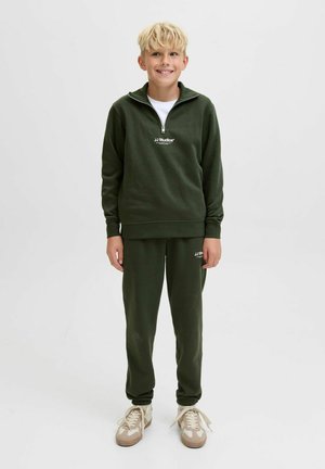 Sudadera verde con media cremallera y logo blanco; pantalones jogger verdes a juego; zapatillas de color claro; textura de tela suave; corte relajado.