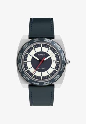 Timex kwarts horloge met een zilveren kast, een marineblauwe lederen band, een witte en marineblauwe wijzerplaat, een rode secondewijzer, en stadsnamen rond de bezel.